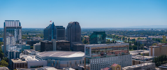 Aerial perspective of Sacramento, California, highlighting the Golden 1 Center, high rise buildings, and the Sacramento River under a clear blue sky.