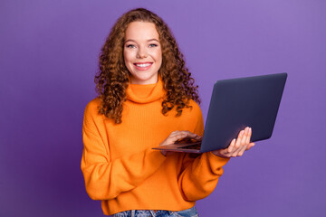 Portrait of pretty young girl hold laptop wear orange sweater isolated on purple color background