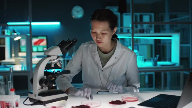 Female food scientist examining sample of cultured meat under microscope while conducting research in laboratory