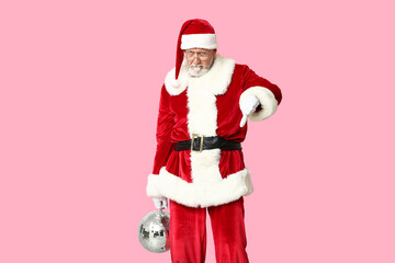 Displeased Santa Claus in glasses with disco ball showing thumb-down gesture on pink background