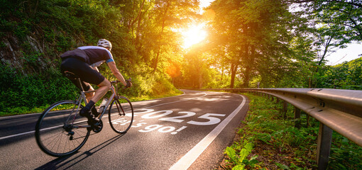 New year 2025 or start straight and beginning concept. Man ride on bike and the number 2025 start written on the road at sunset with lens flare. Concept of challenge or career path, business strategy.