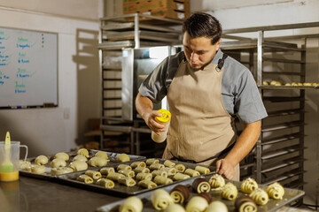 A chef is diligently applying egg wash on several dough pieces on trays, showcasing a crucial step...