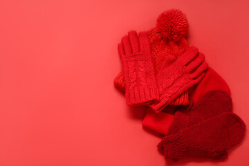 Warm mittens, gloves and hats on red background