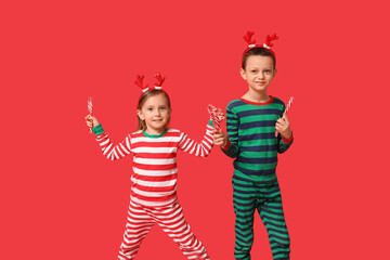 Cute little children in pajamas with candy canes on red background