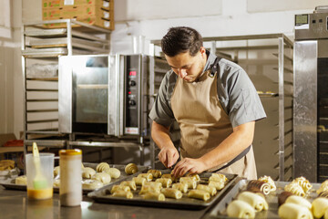 In the bakery setting, a baker intently focuses on intricate pastry preparation steps,...