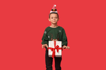 Cute little boy in Christmas sweater with gift on red background