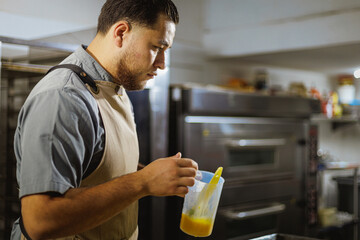 A professional baker, working in a sleek, contemporary kitchen, diligently applies an egg wash to pastries, enhancing the art of baking with both skill and precision amidst an array of tools