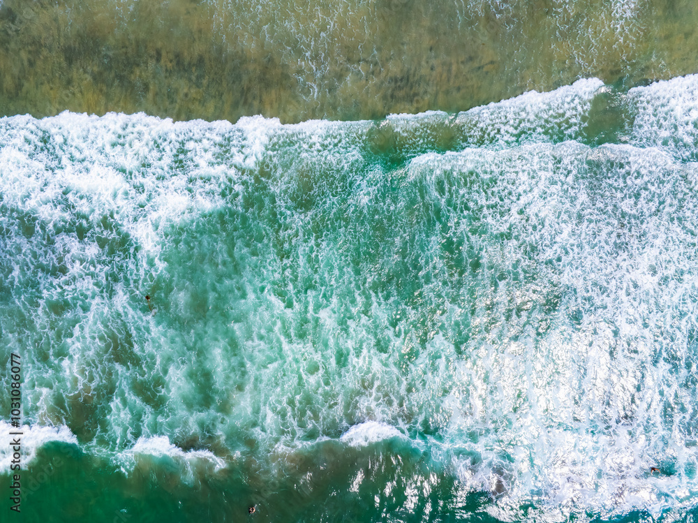 Wall mural Aerial perspective of ocean waves meeting the shore in San Diego, California. Turquoise and emerald waters contrast with white foam, showcasing rhythmic patterns.