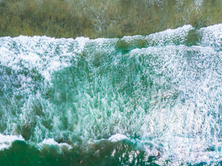 Aerial perspective of ocean waves meeting the shore in San Diego, California. Turquoise and emerald waters contrast with white foam, showcasing rhythmic patterns.