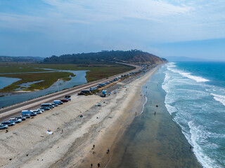 Aerial view of a sandy beach in San Diego, California, with parked vehicles along a road, bordered...