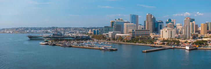 Obraz premium Aerial perspective of San Diego, California, showcasing the skyline, USS Midway Museum, bustling harbor, and rolling hills under a clear blue sky.