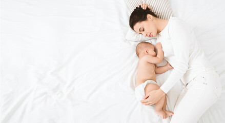 Sweetest dream with baby. Mother embracing her napping baby in bed, sleeping together, top view...