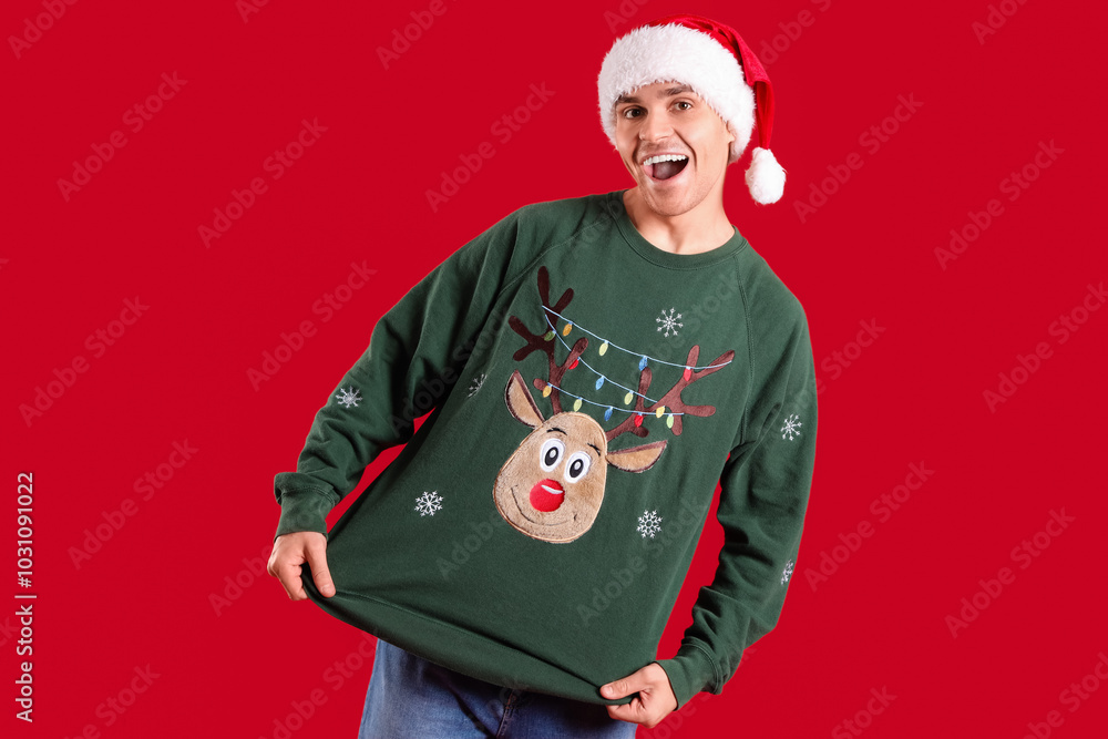 Poster Young man in Santa hat and Christmas sweater on red background