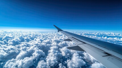Airplane wing above a sea of clouds with a blue sky.