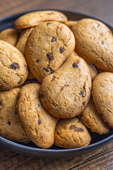 Biscotti frollini con gocce di cioccolato. Chocolate cookies on plate on wooden table.