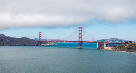 Golden Gate Bridge with Sailboat and Cloudy Sky in San Francisco Bay