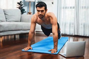Fototapeta premium Athletic and sporty man doing pushup on fitness mat during online body workout exercise session for fit physique and healthy sport lifestyle at home. Gaiety home exercise workout training.