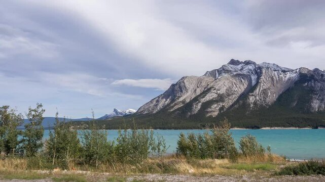 Breathtaking aerial view enormus mountains, blue sky emerald lake in the Rocky mountain in Canada.  People biking along a path on Beautiful nature between lake and mountain. High mountain in sunny day
