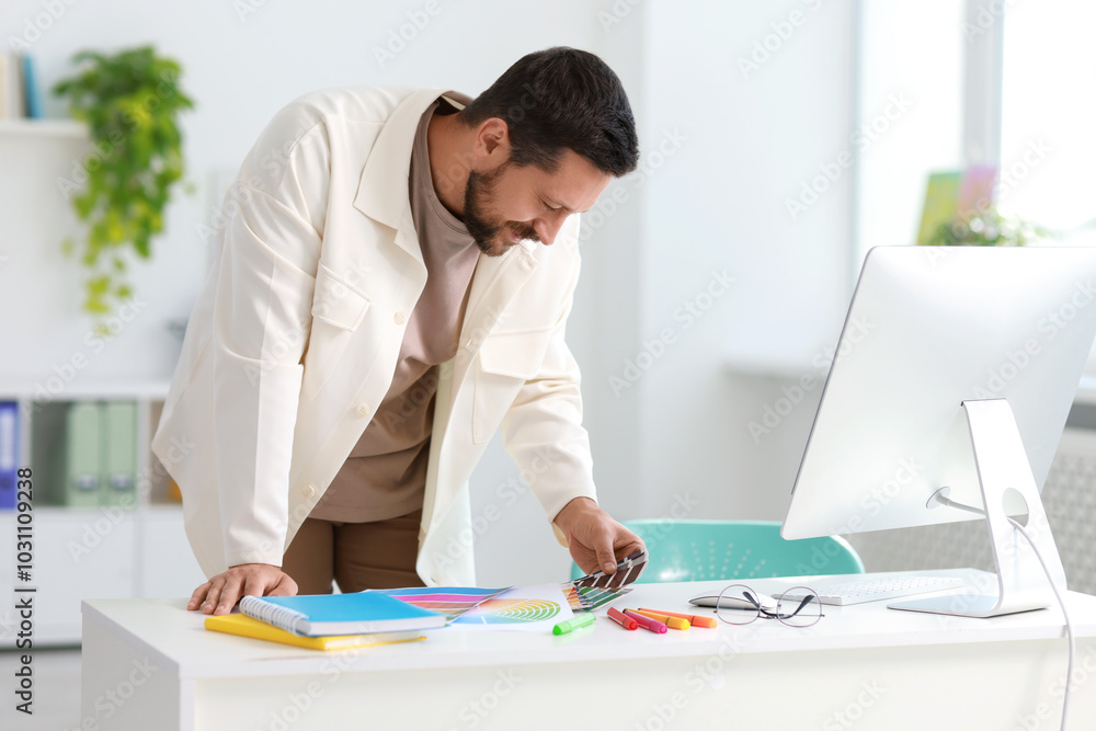 Poster designer with color samples working at table in office