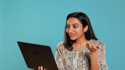 Obraz premium Upbeat woman saluting coworkers, having friendly conversations during teleconference meeting using laptop, studio background. Person discussing during online videocall on notebook device, camera B