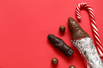 Composition with chocolate Santa Clauses, candies and Christmas gift on red background