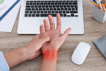 Man suffering from pain in wrist at wooden table with laptop and computer mouse, closeup. Office...