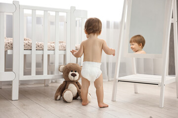 Little child in diaper with teddy bear at home