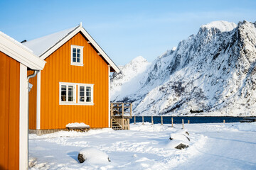 Traditional yellow rorbu house in Sakrisoy fishing village on Lofoten islands, Norway. Winter landscape with snowy mountains and Scandinavian cottage