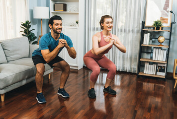 Obraz premium Athletic and sporty couple doing squat together during home body workout exercise session for fit physique and healthy sport lifestyle at home. Gaiety home exercise workout training concept.