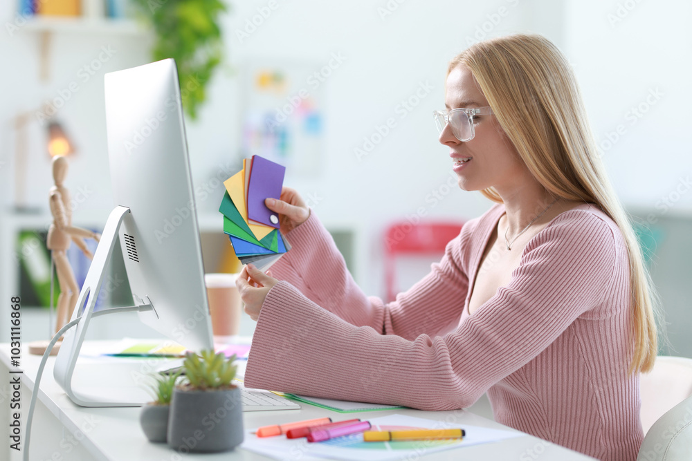 Poster designer with color samples working at table in office