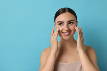 Fototapeta premium Face massage. Beautiful young woman with healthy skin on light blue background, space for text