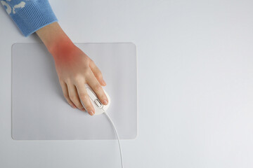 Woman suffering from pain in wrist while using computer mouse at white table, top view. Office...