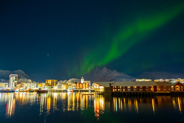 Northern lights over Svolvaer town on Lofoten islands, Norway. Winter night with Aurora borealis, reflection in water, snowy mountains and starry sky. Landscape with polar lights