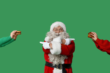 Santa Claus and hands with tasty burgers on green background