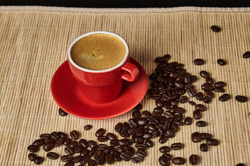 Cup of coffee in the foreground with roasted coffee beans with a light colored mat background