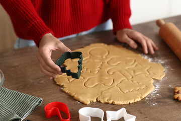 Young woman with cutter making gingerbread cookies in kitchen on Christmas eve, closeup
