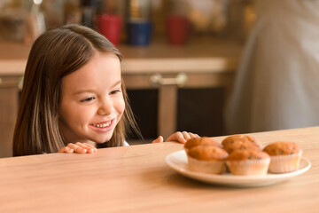 Kids and sweets concept. Adorable little girl craving cookies, looking at sweets in kitchen, panorama with copy space