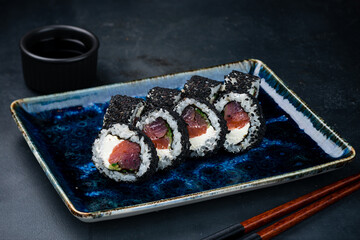 Sushi rolls with tuna, cream cheese, cucumber and sesame seeds, soy sauce and chopsticks.
