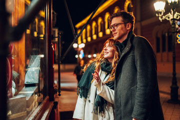 Jolly christmas couple looking at store window with gifts on new year.