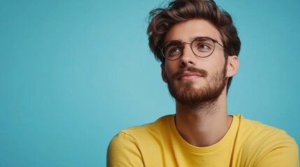 Fototapeta premium Thoughtful Young Man in Yellow Shirt Against Blue Background