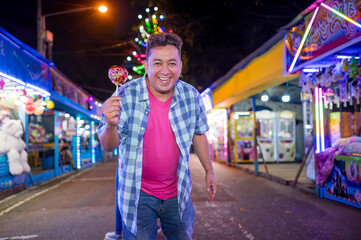 A visitor to the fair takes a picture and smiles profusely, carrying a red caramel apple topped with various sweets.