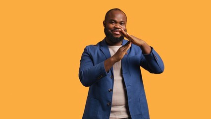 Cheerful african american man asking for timeout, doing hand gestures, halting activities. Friendly upbeat person doing pause sign gesturing, wishing for break, studio background, camera B