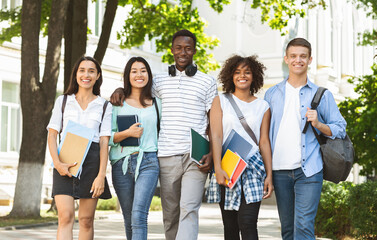 Obraz premium Cheerful college students walking out of campus together, and posing at camera outdoors, having break in classes, free space