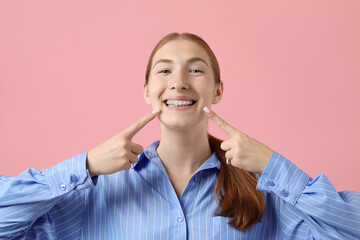 Girl pointing at her braces on pink background