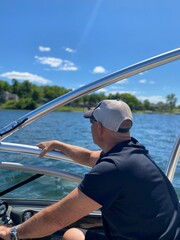 Man looking out onto the lake piloting a ski boat with blue sky and white clouds.