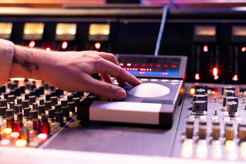 Skilled sound engineer operating mixing console and motorized faders in studio, using technical...