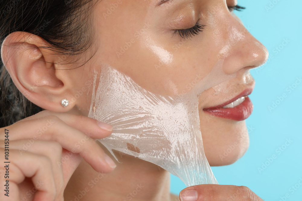 Poster Smiling woman peeling off face mask on light blue background, closeup