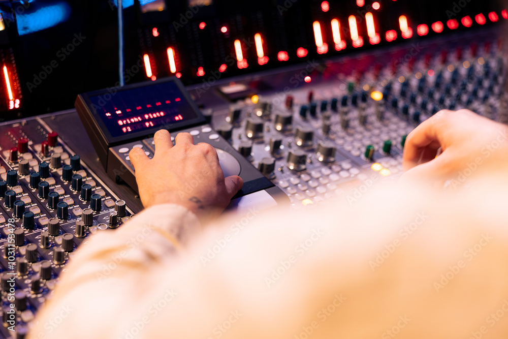 Fototapete Tracking engineer pressing faders and buttons on control desk to balance sounds and add effects in post production, creating new music. Technical expert working with sliders in professional studio.