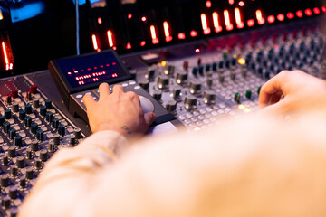 Tracking engineer pressing faders and buttons on control desk to balance sounds and add effects in...