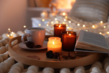 Burning candles, lights, coffee, book and decor on bed indoors, closeup. Autumn atmosphere